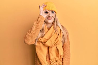 Beyaz kadın yün kazak ve şapka giyiyor. El hareketleriyle gülümsüyor. Gözleri mutlu yüzüyle parmaklarının arasından bakıyor.. 