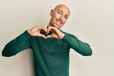 Kel, sakallı, balıkçı yaka kazak giyen, aşka gülümseyen, elleriyle kalp sembolü yapan bir adam. romantik kavram. 