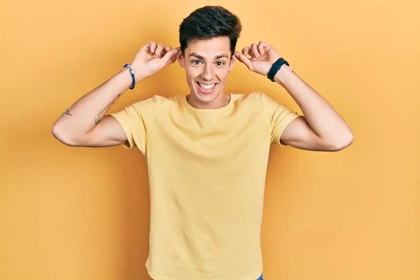 Sarı Bir Tişört Giyen Genç Spanyol Adam Gülümsüyor Kulakları Parmaklarıyla — Stok fotoğraf