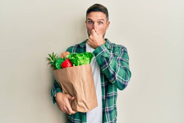 Sakallı yakışıklı bir adam. Elinde poşet dolusu yiyecek var. Kokuşmuş ve iğrenç bir koku var. Kötü kokuyor. 