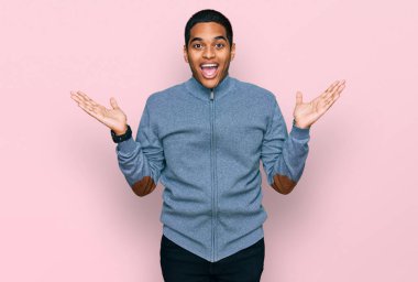 Genç, yakışıklı, sıradan bir tişört giyen, çılgın ve başarıyı kolları açık, gözleri açık, heyecanlı bir şekilde kutlayan İspanyol bir adam. Kazanan konsept 