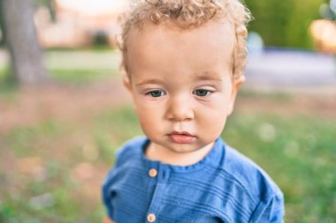 Sevimli ve mutlu küçük çocuk güneşli bir günde parkta eğleniyor. Güzel sarı saçlı erkek çocuk dışarıda oynuyor.