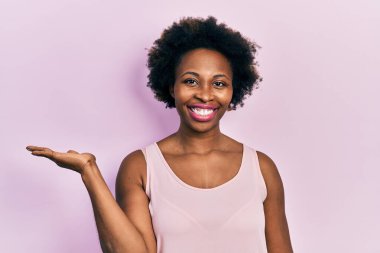 Genç Afro-Amerikalı kadın kolsuz tişört giyiyor neşeli bir şekilde gülümsüyor ve avuç içi kameraya bakıyor.. 