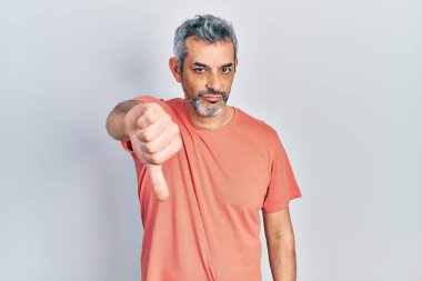 Yakışıklı, orta yaşlı, gri saçlı, sıradan tişörtlü mutsuz ve sinirli görünen, reddedilmiş ve baş parmakları aşağıda hareket eden bir adam. kötü ifade. 