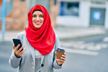 Genç Arap iş kadını akıllı telefon kullanıyor ve şehirde kahve içiyor..