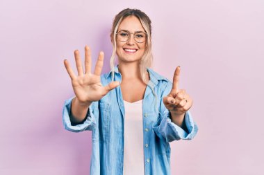 Güzel, genç, sarışın bir kadın. Günlük kıyafetler ve gözlük takıyor. Altıncı parmaklarıyla gösteriyor ve işaret ediyor.. 