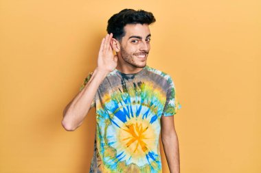 Gündelik kıyafetler giyen, ağzı kulaklarında gülümseyen genç İspanyol bir adam dedikoduları ve dedikoduları dinliyor. Sağırlık kavramı. 