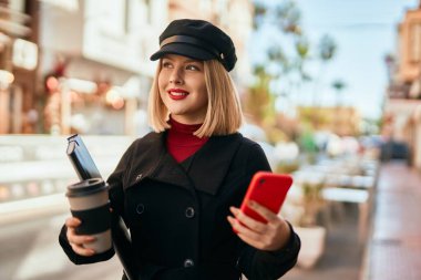 Genç sarışın kadın şehirde kahve içerken akıllı telefon kullanıyor..