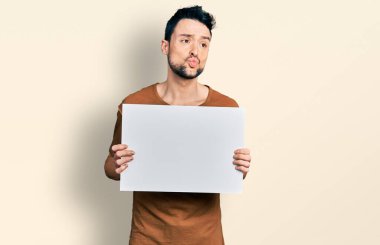 Sakallı, boş afiş taşıyan İspanyol bir adam kameraya bakıp öpüşürken çok güzel ve seksi görünüyor. aşk ifadesi. 