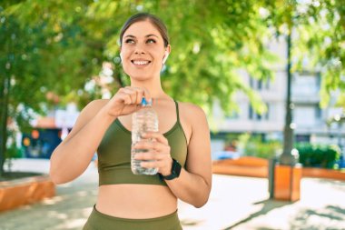 Genç sarışın sporcu şehirde bir şişe su içerek egzersiz yapıyor..