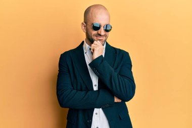 Moda güneş gözlüğü takan ve iş ceketi giyen genç İspanyol adam kameraya kollarını kavuşturup, çenesini kapatarak gülümsüyor. Olumlu düşünmek. 