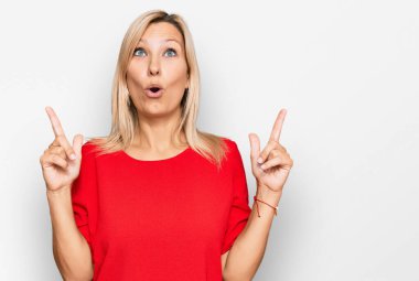 Orta yaşlı, günlük kıyafetler giyen beyaz bir kadın şaşkın şaşkın yukarı bakıyor, parmaklarıyla işaret ediyor ve kollarını kaldırıyordu.. 