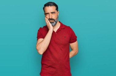 Orta yaşlı, sakallı, normal kırmızı tişörtlü, yorgun ve bunalımda kollarını kavuşturmaktan sıkılmış görünen bir adam.. 