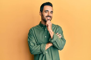 Gündelik giysiler giyen genç İspanyol adam kameraya kollarını kavuşturup çenesine dokunarak gülümsüyor. Olumlu düşünmek. 