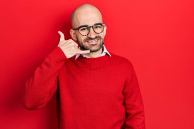 Genç kel bir adam günlük kıyafetler ve gözlük takıyor gülümsüyor telefonla el ve parmak hareketleri yapıyor telefonda konuşuyor gibi. iletişim kavramları. 