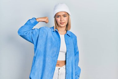 Güzel sarışın kadın yün şapka takıyor güçlü biri kol kası gösteriyor, kendinden emin ve gururlu. 