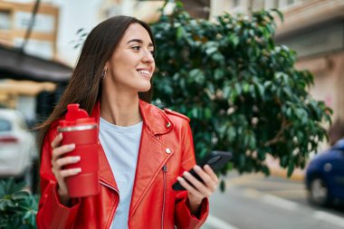 Genç İspanyol kadın akıllı telefon kullanıyor ve şehirde kahve içiyor..