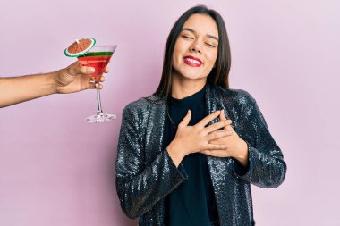Seksi parti ceketi giyen genç bir kız ve İspanyol kollu bir kokteyl sunan elleri göğsünde gülümseyen, gözleri kapalı, yüzünde minnet ifadesi olan bir kız. sağlık kavramı. 