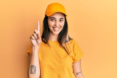 Teslimat üniforması giyen, şapkalı genç İspanyol kadın bir numarayı gösterip işaret ederken kendinden emin ve mutlu bir şekilde gülümsüyor.. 