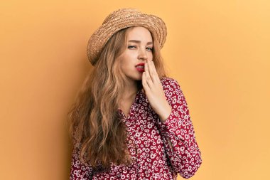 Yazlık şapka takan güzel, sarışın, beyaz bir kadın ağzıyla ağzını kapatmaktan sıkılmış. Huzursuz ve uykulu.. 