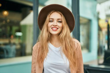 Genç sarışın kız gülümsüyor, mutlu bir şekilde şehirde duruyor..