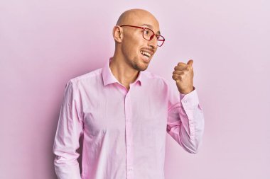 Kel, sakallı, günlük kıyafetler giyen, gözlüklü, baş parmağını kaldıran, ağzı açık gülümseyen bir adam. 