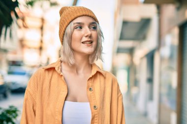 Genç sarışın kız gülümsüyor, mutlu bir şekilde şehirde duruyor..