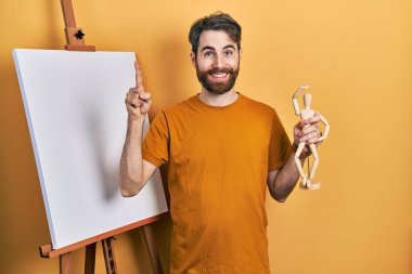 Kafkasyalı sakallı bir adam elinde bir fikir ya da soruyla şaşırmış bir manikinle resim sehpasının yanında duruyor. 