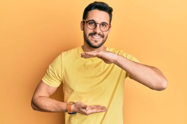 Gündelik kıyafetler giyen ve büyük boy ve ölçü işareti gösteren el kol hareketleri yapan Latin kökenli genç bir adam. Kameraya bakıp gülümsüyor. ölçüm kavramı. 