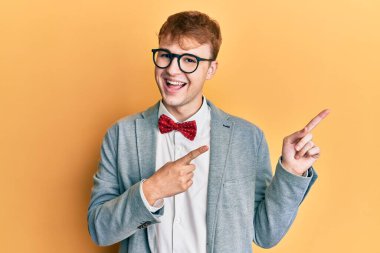 Genç, beyaz, inek, gözlüklü, hippi görünümlü, papyon takan, gülümseyen ve kameraya bakan iki eli ve parmağı yanda olan bir adam.. 