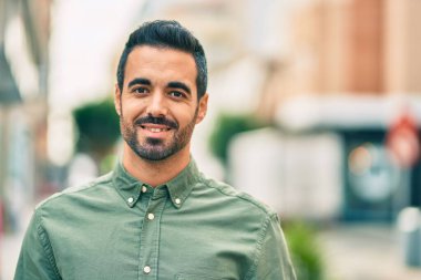 Genç İspanyol adam gülümseyerek şehirde mutlu mesut dikiliyor..