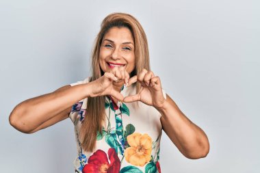 Orta yaşlı İspanyol kadın, gündelik giysiler giyip, sevgiyle gülümsüyor. Kalp sembolü ve elleri ile şekil veriyor. romantik kavram. 