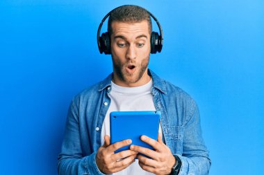 Genç beyaz adam kulaklık takıyor. Kulaklık takıyor. Şaşırmak için ağzı açık kalmış, korkmuş ve şaşkın. 