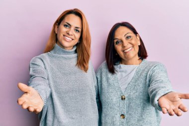 Latin anne ve kız günlük kıyafetler giyip neşeli gülümseyerek avuç içi yardım ve kabul vaadinde bulunuyorlar.. 