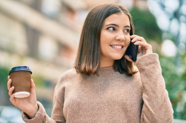 Genç İspanyol kadın akıllı telefonda konuşuyor parkta kahve içiyor..