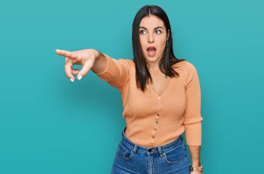 Gündelik giysiler giyen genç İspanyol kadın parmağıyla işaret ederek şaşırmış, ağzı açık, şaşırmış, ön tarafta bir şey var. 
