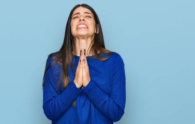 Genç İspanyol kadın gündelik giysiler giyip elleri bağlı yalvarıyor ve dua ediyor. Yüzünde umut ifadesi var. Çok duygusal ve endişeli. Yalvarıyor. 