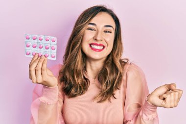 Genç İspanyol kız elinde haplarla gururla bağırıyor zaferi kutluyor ve başarıyı kollarını kaldırarak kutluyor. 