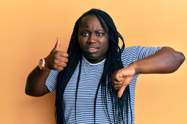 Örgülü genç siyahi kadın parmaklarını eğip parmağını kaldırıyor. Hiçbir şeyden habersiz ve kafası karışık bir ifade sergiliyor. şüphe kavramı. 