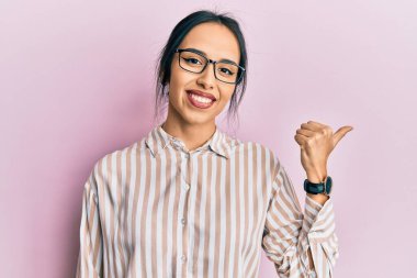 Gündelik kıyafetler giyen ve gözlüklü genç İspanyol kız baş parmağını yana kaldırmış, ağzı açık gülümsüyor. 