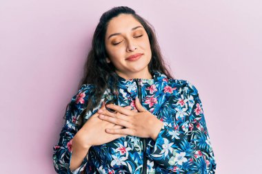 Güzel bir ortadoğulu kadın, sıradan bir çiçek ceketi giyiyor, elleri göğsünde, gözleri kapalı gülümsüyor ve yüzünde minnet ifadesi var. sağlık kavramı. 