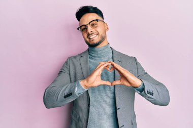 Genç Arap adam, iş kıyafetleri giymiş, aşık gülümseyen, elleriyle kalp sembolü yapan. romantik kavram. 
