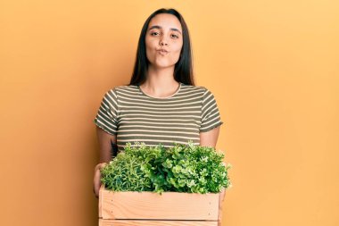 Genç İspanyol kadın elinde tahta bir saksı tutarken kameraya bakıyor ve öpüşürken sevimli ve seksi oluyor. aşk ifadesi. 