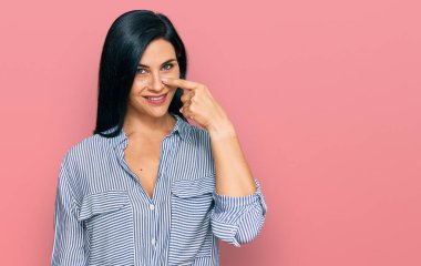 Kafkasyalı genç bir kadın, günlük kıyafetler giyip, el ve burnu işaret ediyor, neşeli bir şekilde gülümsüyor. güzellik konsepti 