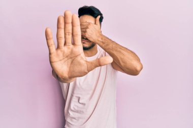 Genç Arap adam gündelik giysiler giyip elleri ile gözleri kapatıyor ve üzgün ve korku ifadeleriyle jest yapıyor. utangaç ve olumsuz kavram. 