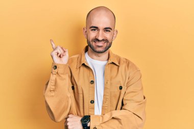 Gündelik kıyafetler giyen genç kel adam gülümseyerek mutlu bir şekilde elini ve parmağını kenarda gezdiriyor. 