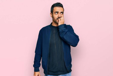 Günlük kıyafetler giyen genç İspanyol adam gergin ve gergin görünüyor. Ağzı tırnak yiyen eller. anksiyete. 