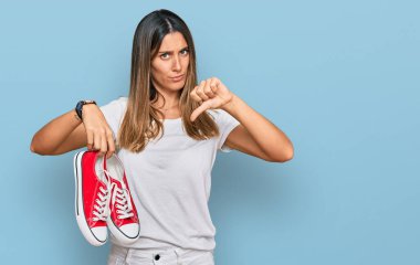 Kızgın yüzlü, kırmızı ayakkabılı genç bir kadın, olumsuz işaretli baş parmakları aşağıda, reddedilme konsepti. 