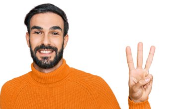 Gündelik kıyafetler giyen genç İspanyol adam üç numarayı gösterip işaret ederken kendinden emin ve mutlu gülümsüyor.. 