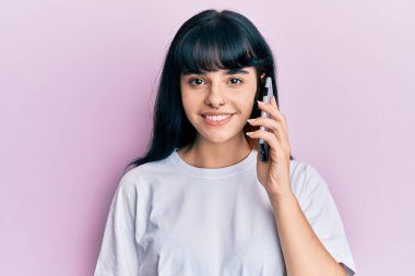 Genç İspanyol kız akıllı telefondan konuşuyor. Olumlu ve mutlu görünüyor. Kendine güvenen bir gülümsemeyle dişlerini gösteriyor. 